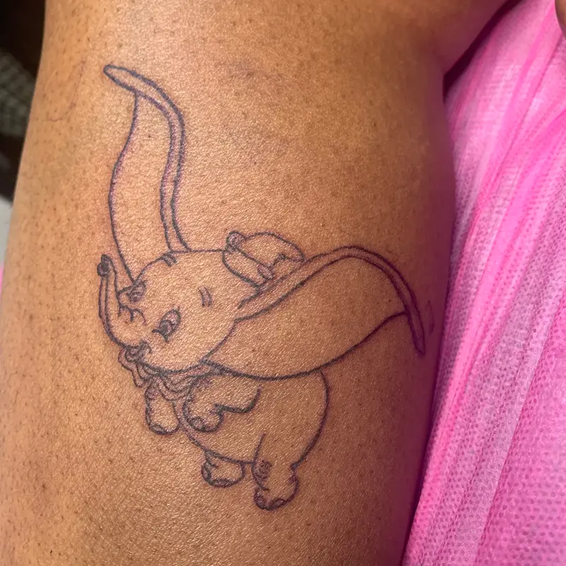Fine-line outline tattoo of Dumbo the flying elephant on the leg, by Andres at Killer Silver Tattoo