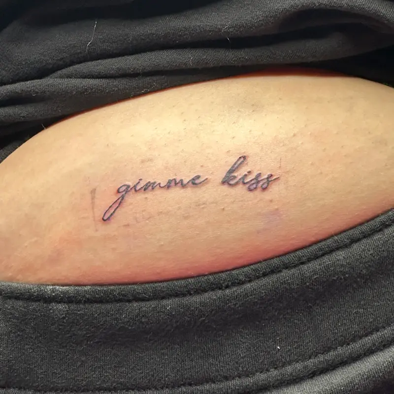 Fine-line script lettering tattoo reading "gimme kiss," by Andres at Killer Silver Tattoo