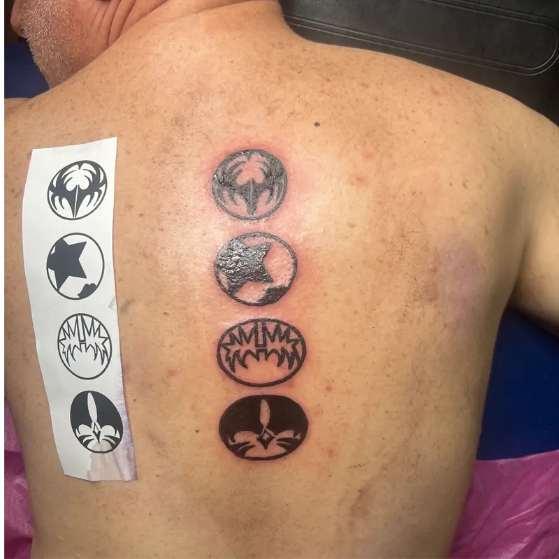 Blackwork tattoo of the four KISS member emblems stacked down the spine, by Andres at Killer Silver Tattoo