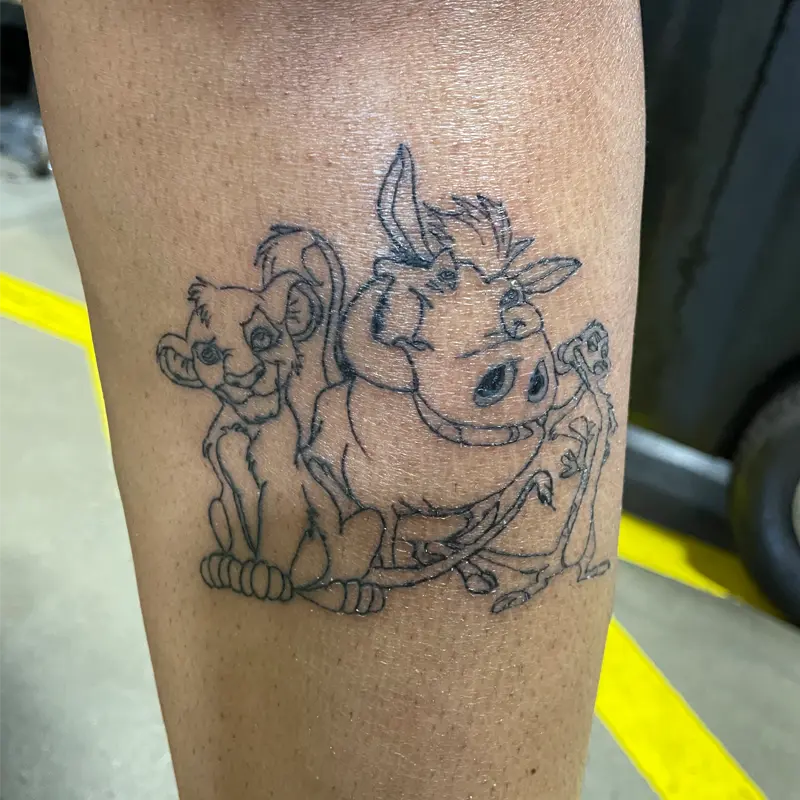 Fine-line outline tattoo of Simba, Pumbaa and Timon from The Lion King on the leg, by Andres at Killer Silver Tattoo