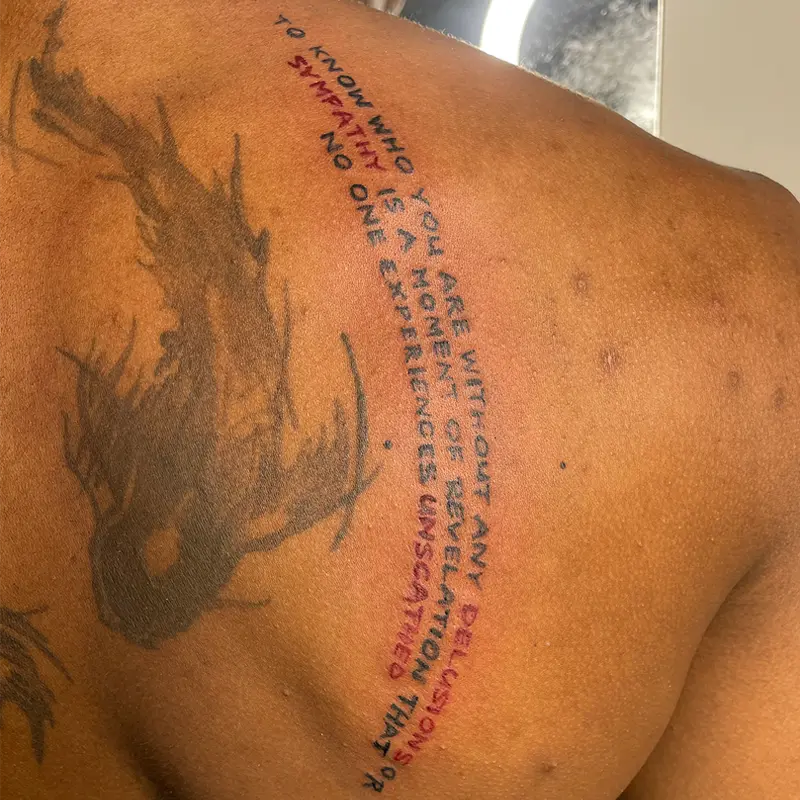 Black and red quote lettering tattoo on the shoulder blade, by Andres at Killer Silver Tattoo