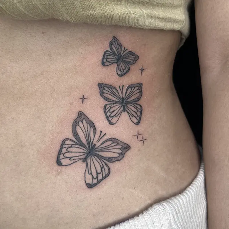 Illustrative blackwork butterfly trio tattoo with star accents on ribcage — Killer Silver Tattoo Studio