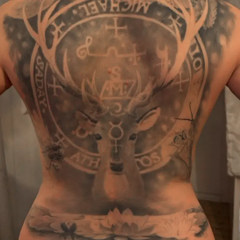 Black and gray realism back piece of a stag framed by the sigil of Archangel Michael, with a praying mantis, dragonfly and lotus flowers