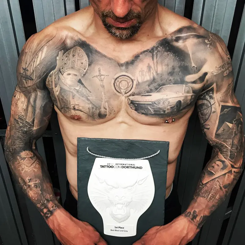 Black and gray realism chest piece and full sleeves; client holds the 1st Place Best Black and Grey plaque from Tattoo Convention Dortmund, Germany