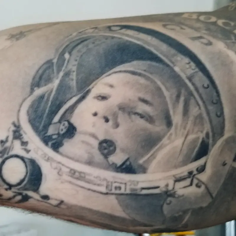 Black and gray realism portrait tattoo of Jurij Gagarin in a Soviet cosmonaut helmet marked CCCP