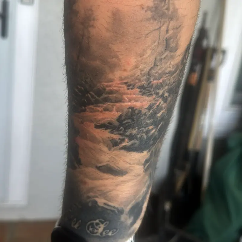 Black and gray realism tattoo of a misty forest creek flowing over rocks on the forearm, part of a full sleeve