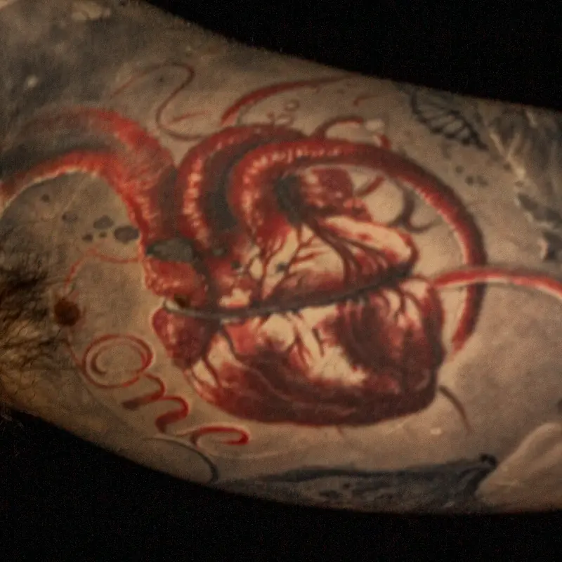 Realistic red anatomical heart tattoo with "One" in script, part of a black and gray life-themed sleeve by Caesar The Hun