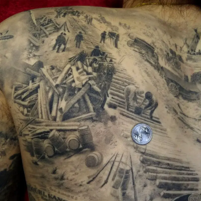 Black and gray realism back piece of 19th-century workers laying railroad track near a Native American camp, a coin shown for scale