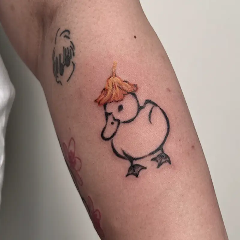 Small illustrative fine-line duck tattoo with orange flower hat on detail on arm — Killer Silver Tattoo Studio
