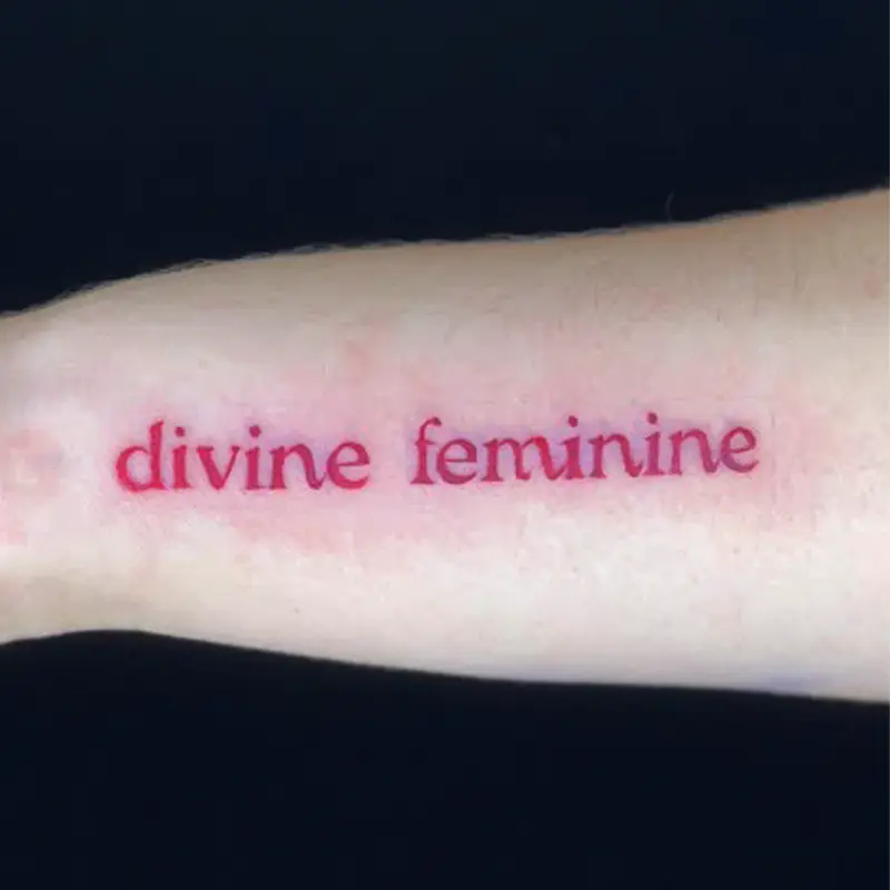 "Divine feminine" script lettering tattoo in red ink on forearm — Killer Silver Tattoo Studio
