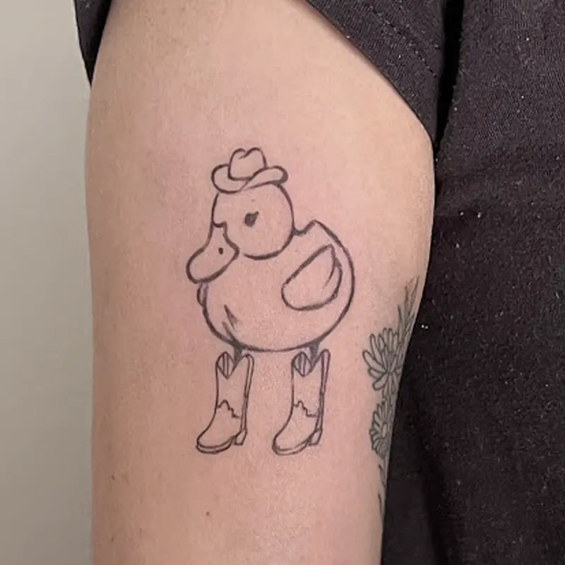 Fine-line cartoon duck tattoo wearing a cowboy hat and boots, on upper arm — Killer Silver Tattoo Studio