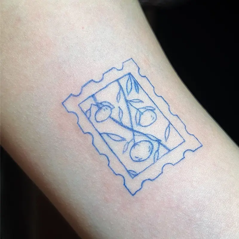 Fine-line postage stamp tattoo with citrus branch, blue ink, on forearm — Killer Silver Tattoo Studio