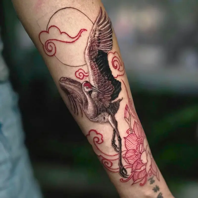 Asian fusion forearm tattoo of a red-crowned crane in flight with cloud linework, by Philipus