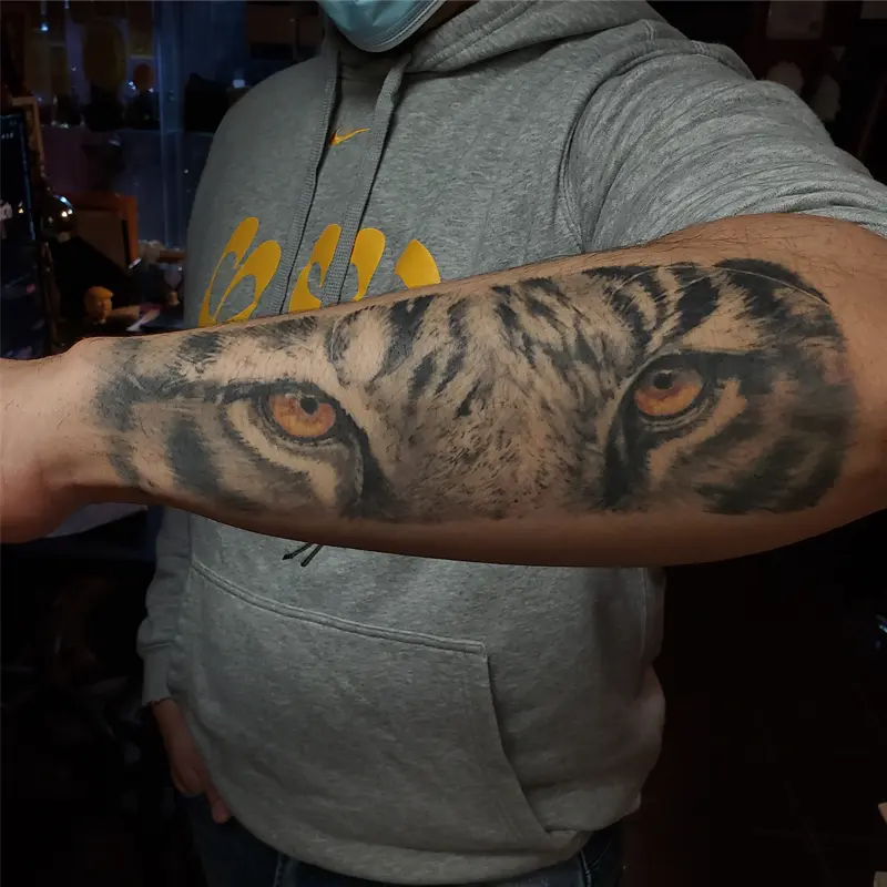 Black and gray realism forearm tattoo of a tiger's eyes, by Philipus