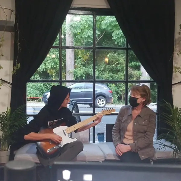 Clients relaxing and playing guitar in the front window seat at Killer Silver Tattoo Studio in Scarsdale, NY